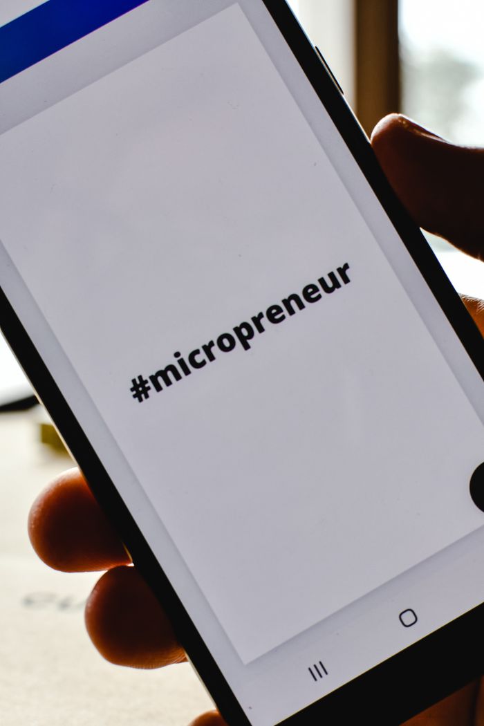 Gros plan sur une main tenant un smartphone affichant le hashtag #micropreneur à l’écran, symbole de l’entrepreneuriat.